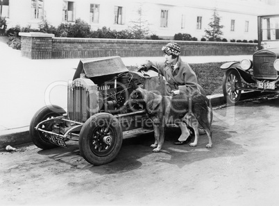 Young woman sitting next to small car looking at the engine with her German shepherd