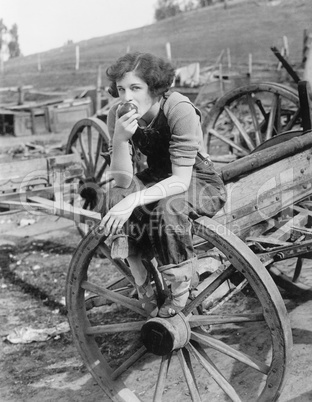 Young woman in working jeans sitting on wheel eating an apple