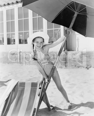 Girl placing a large umbrella into the sand