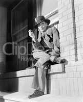 Young woman in men's clothing sitting on a window ledge smoking a pipe