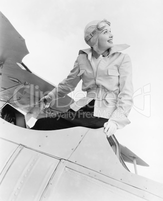 Young woman sitting on top of a biplane with gargles and hat