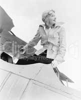 Young woman sitting on top of a biplane with gargles and hat