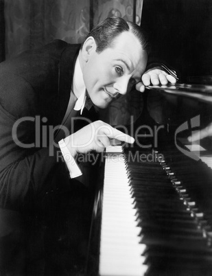 Man leaning over the piano playing the keys with one finger