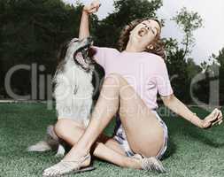Young woman sitting on a lawn and singing with her dog