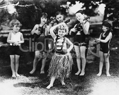 Group of children performing with instruments and one girl dancing the hula