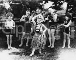 Group of children performing with instruments and one girl dancing the hula