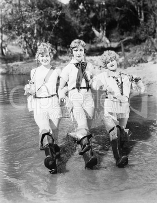 Three woman walking with fishing rods through a stream