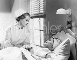 Nurse comforts a patient in a hospital bed, talking to each other