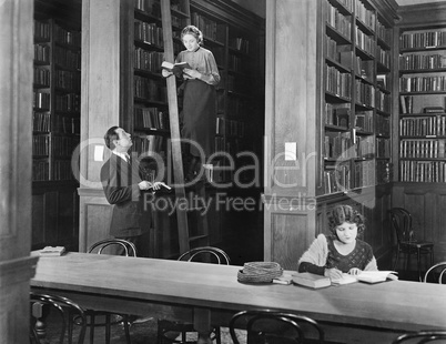 Man talking to a woman standing on a ladder in a library