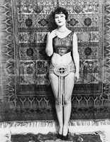 Young woman barely dressed in front of a hanging carpet