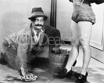 Man cleaning the floor looking at the legs of a woman