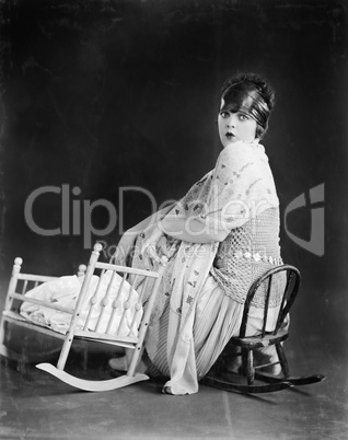 Young woman sitting on a toy chair next to a toy baby crib