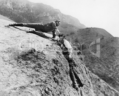 Man helping another man from falling down a cliff