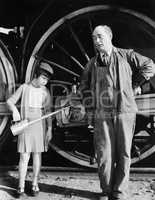 Little girl with an oil can standing next to a locomotive and the engine driver