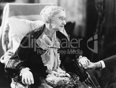 Elderly woman sitting in a chair holding a man's hand