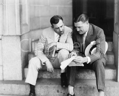 Two men sitting on steps and reading a document