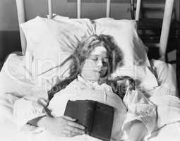 Young woman lying in bed, sleeping and holding a book
