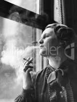 Young woman sitting next to window, smoking