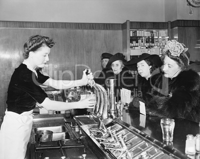 Three woman and a man sitting in a soda fountain