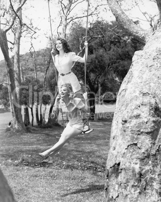 Two women sitting and standing on a swing