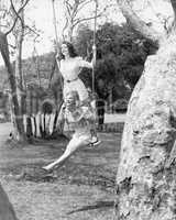 Two women sitting and standing on a swing