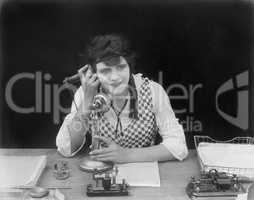 Young woman sitting at her desk in an office with a telephone in her hands