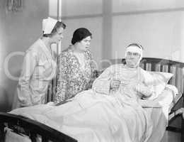 A wife next to her husband in a hospital bed with a nurse attending