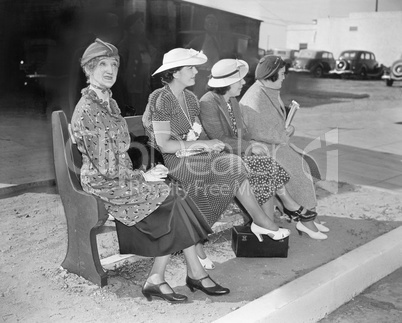 Four women sitting on a bench waiting for the bus