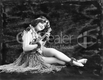 Young woman playing guitar in a Hawaiian grass skirt