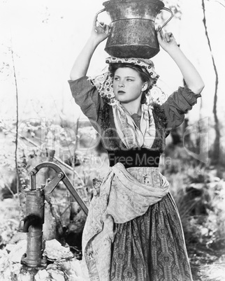 Young woman with water bucket on her head next to a well