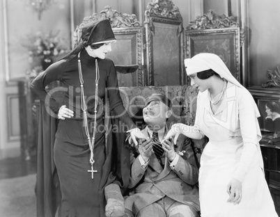 Young man with an eye patch being consoled by a nurse and a religious woman