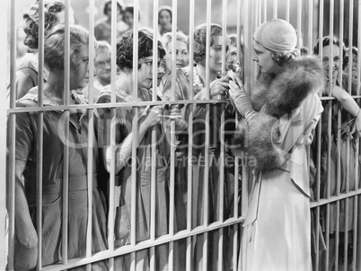 One woman standing in front of a jail talking with a group of women