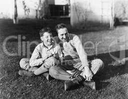 Father and son sitting together on the grass in the back yard