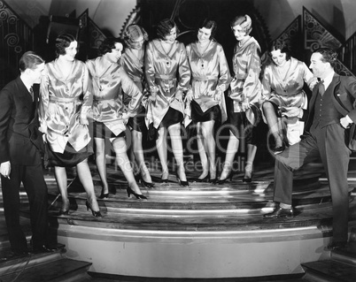 A chorus line of women showing off their legs to two men