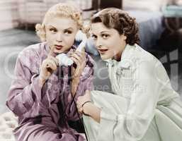 Two women sitting together and listening on the telephone receiver