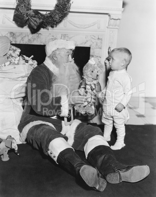Santa Claus with a little boy and a teddy bear in front of a fire place