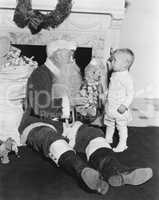 Santa Claus with a little boy and a teddy bear in front of a fire place