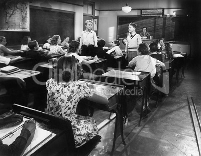 Children in a class room with a teacher and two boys looking at each other