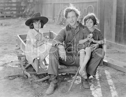 Father sitting with his two daughters on a small wagon on a farm