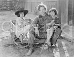 Father sitting with his two daughters on a small wagon on a farm