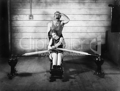 Woman sitting on a rowing machine with a man behind her