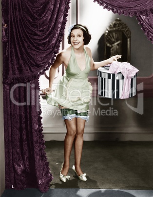 Woman walking into a room wearing lingerie and holding a hat box