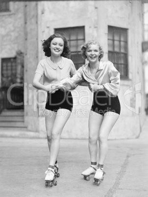 Two young women with roller blades skating on the road and smiling