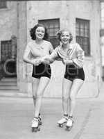 Two young women with roller blades skating on the road and smiling