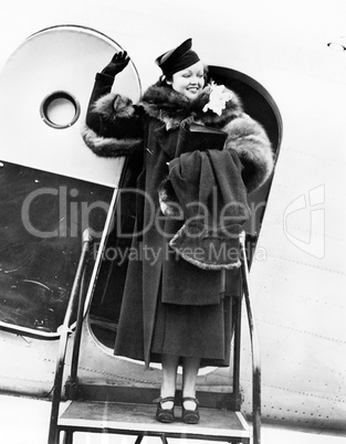 Elegant woman stepping out of an airplane and waving