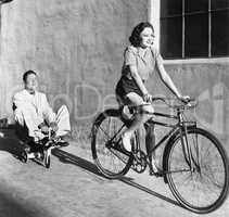 Woman on a bicycle pulling a grown man on a toy tricycle