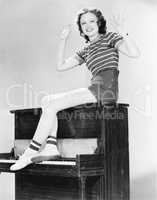 Woman sitting on top of a piano waving her arms