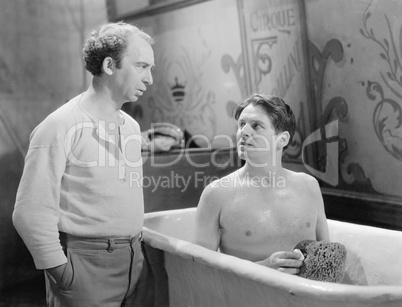 Two men talking while one sitting in a bathtub