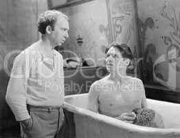 Two men talking while one sitting in a bathtub