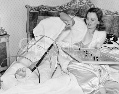 Woman in bed trying to scratch her broken foot with a pole